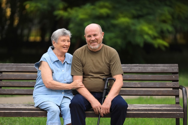 Happy elderly man and disabled woman sitting on bench outdoors
