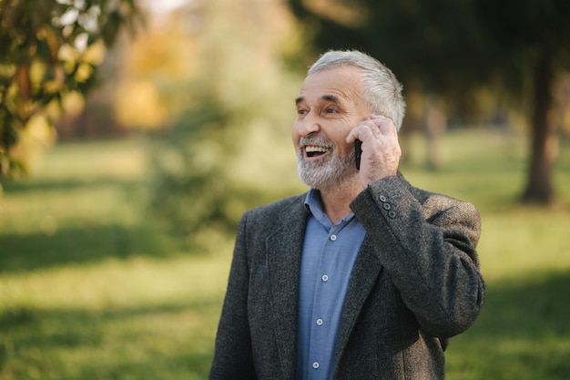 Happy elderly man speak with somebody by the phone Handsome senior man with beautiful beard smile