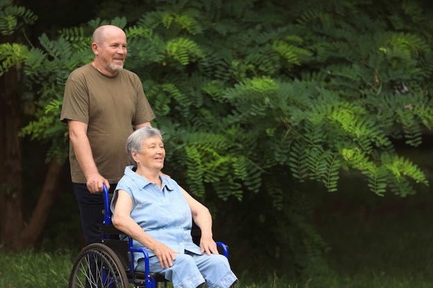 Happy elderly man walking with disabled elderly woman sitting in wheelchair