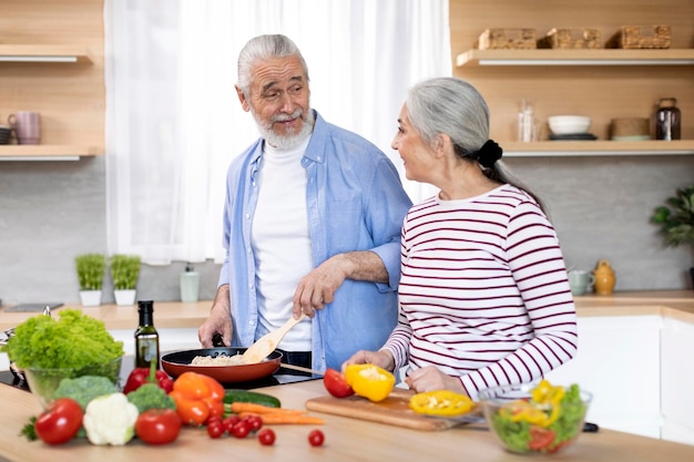 Happy elderly spouses cooking lunch meal together in kitchen