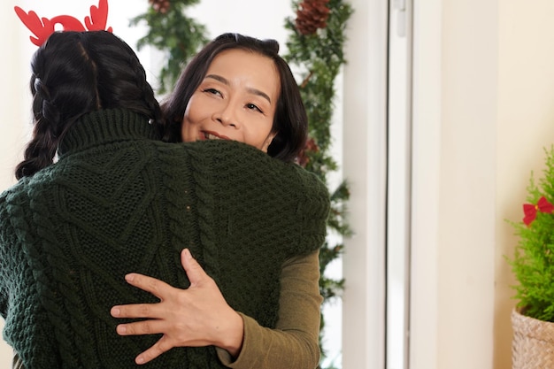 Happy elderly woman hugging her adult daughter in reindeer antlers and warm sweater