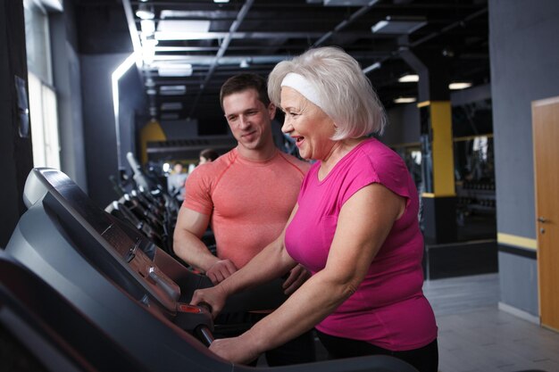 Donna anziana felice che ride mentre fa esercizio cardio sul tapis roulant con il suo personal trainer