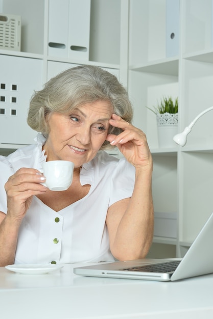 Donna anziana felice che lavora al computer portatile in ufficio