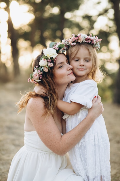 Photo happy elegant mother and her beautiful daughter with flower wreaths in a park at sunset