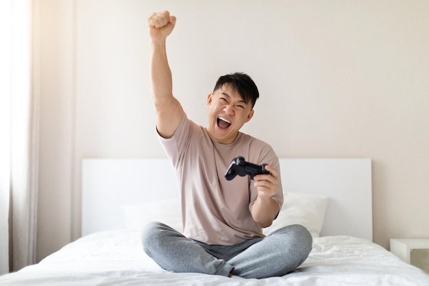 Happy emotional asian man playing video games at home