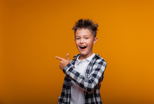 Happy emotional boy surprised shows something with his finger on blue background