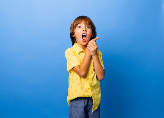 Happy emotional boy surprised, shows something with his finger on blue background