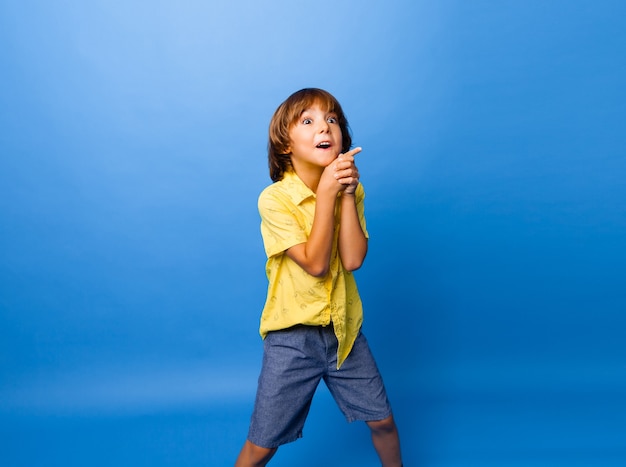 Happy emotional boy surprised, shows something with his finger on blue background