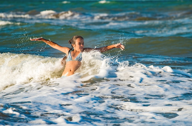 幸せな感情的な少女は、晴れた暖かい夏の日に泡立つ嵐の海の波を浴びます