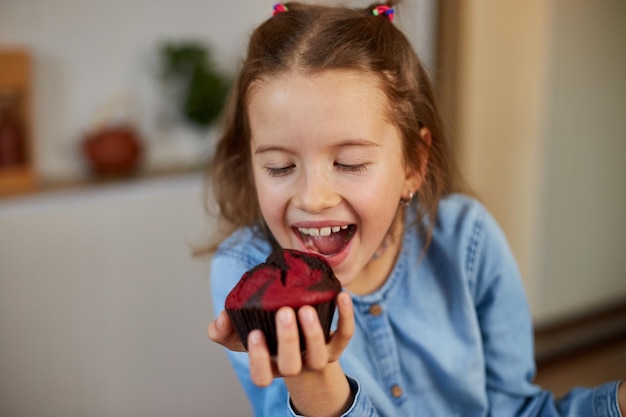 Happy emotional little girl eats cupcake at home