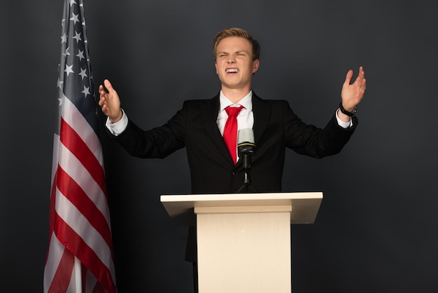 Happy emotional man on tribune with american flag on black background
