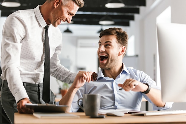 Happy emotional men colleagues in office working with computer.