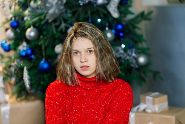 Happy emotional surprised young woman by a Christmas tree in cozy living room, concept of happiness