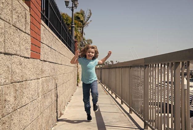幸せなエネルギッシュな男の子の子供は、夏休みの自由の間に遊歩道を走る自由な時間をお楽しみください