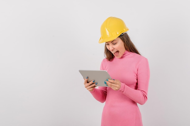 Happy engineer girl is screaming by looking at tablet computer on white background