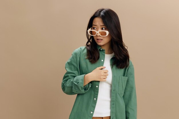 Happy enjoyed korean young woman in khaki green shirt stylish\
eyewear looks aside posing isolated on over beige pastel studio\
background cool fashion offer sunglasses ad concept