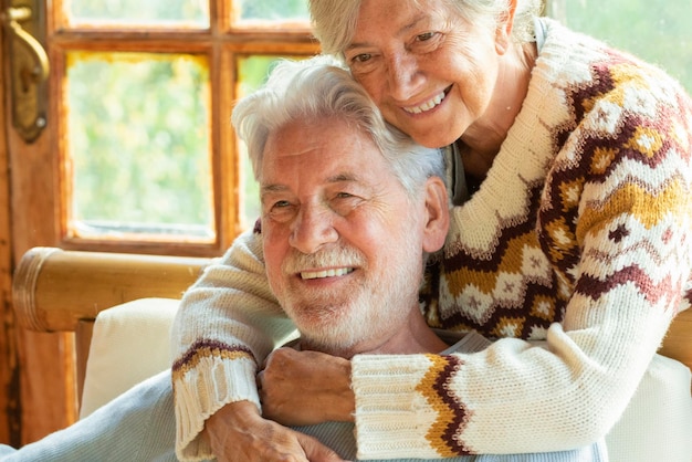 Happy and enjoyed senior caucasian couple smile and hug each other sitting on a chair in cozy home cabin chalet two man and woman old elderly people lifestyle enjoying relax and relationship