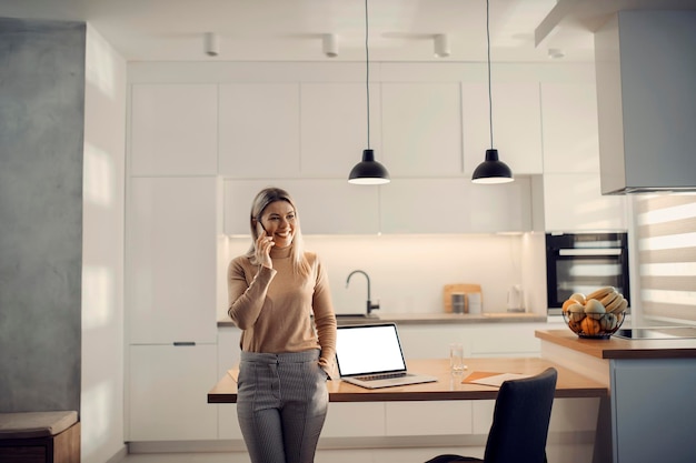 A happy entrepreneur having a phone call in kitchen at her home