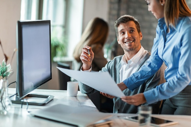 Happy entrepreneurs talking to his female colleague while analzying business plan in the office Focus is on man