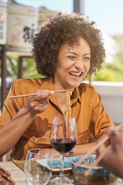 レストランのテラスでチョップスティックでヌードルを食べ ⁇ 赤ワインを飲んでいるブラウスを着た幸せな民族のカモい ⁇ の女性