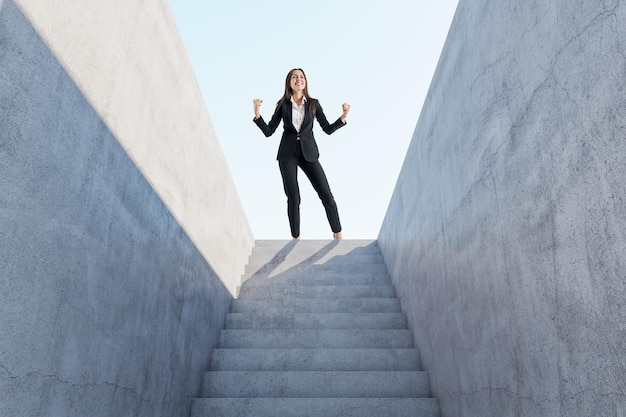 햇빛 성장과 리더십 개념으로 추상 콘크리트 계단 꼭대기에서 성공을 축하하는 행복한 유럽 여성 사업가
