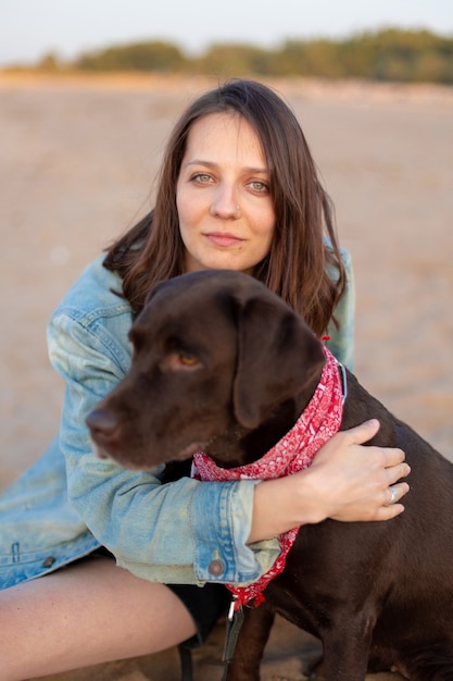 Happy european country woman with dark hair in a vintage denim jacket hugging a dog and smiling