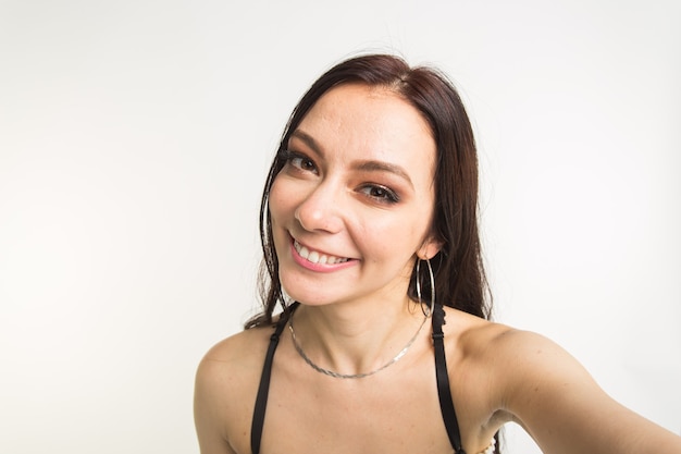 Happy european female model with dark hair. young woman is taking a selfie on white wall.