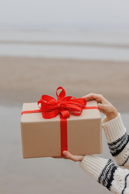 A happy European woman in a Santa Claus hat holds a gift in a box with a red ribbon