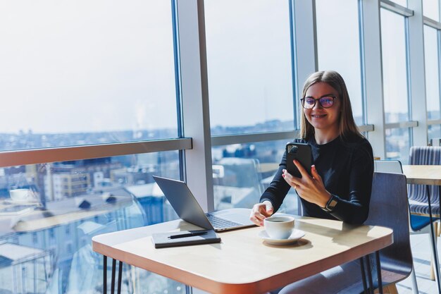 Happy european woman working online in cafeteria using laptop and coffee copy space Successful female freelancer typing on laptop remote work