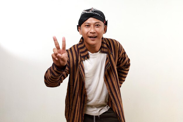 Happy excited asian adult man in javanese costume standing while showing two fingers Victory concept