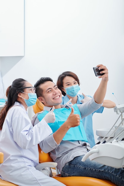 Happy excited Asian man smiling and taking selfie with dentist and assistant