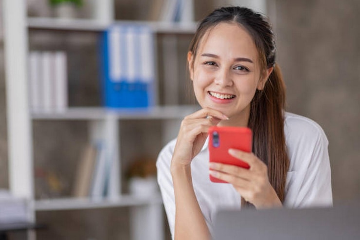 Photo happy excited asian young entrepreneur business woman using phone and laptop sitting on a desk offic