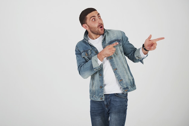 Happy excited bearded man in eyeglasses looking at camera with smile and pointing away at copy space with two fingers isolated over white background.