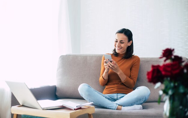 Happy excited beautiful woman with smart phone on the couch