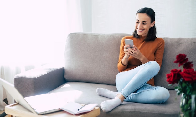 Happy excited beautiful woman with smart phone on the couch