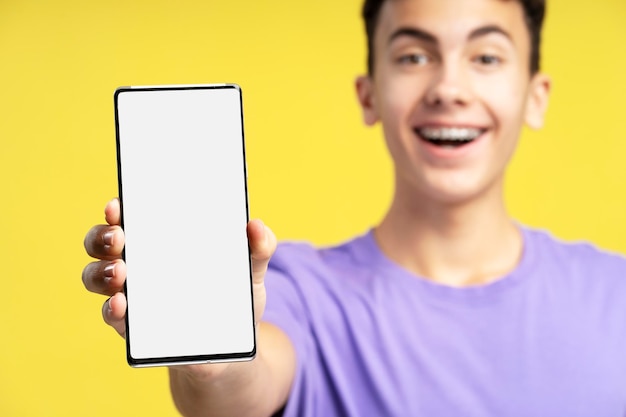 Happy excited boy teenager holding mobile phone showing blank white screen selective focus closeup