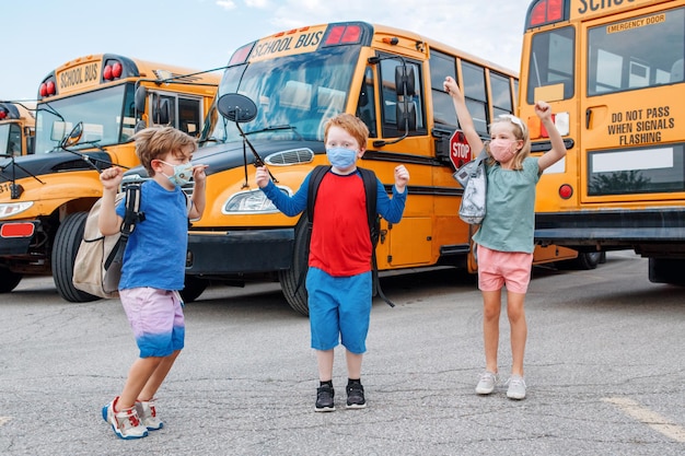 Photo happy excited children kids students in protective face masks jumping near school yellow bus