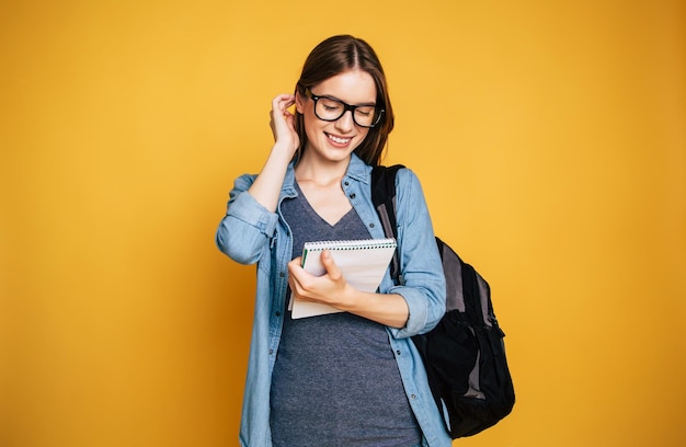 Happy and excited cute young student girl portrait in glasses with backpack isolated in studio