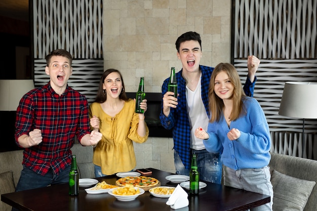 피자를 먹고 알코올 음료를 마시는 술집에서 TV에서 축구를보고 행복 흥분 즐거운 네 친구