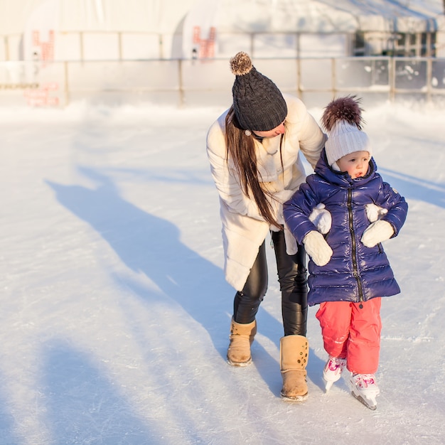 Happy excited little girl and her young mother learning ice-skating