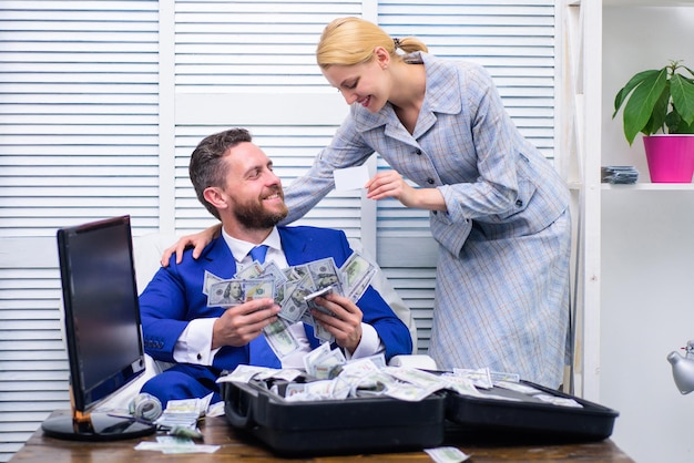 Happy and excited man sitting at table covered with money and rejoices with girl secretary