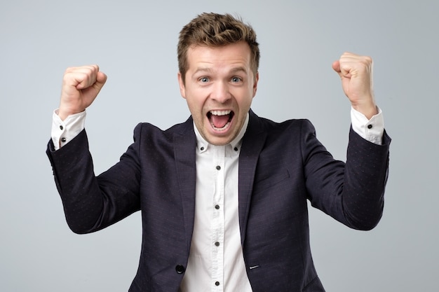 Happy excited man in suit screaming and celebrating succcess with two fists up