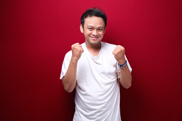 Happy excited and smiling young Asian man raising his arm up to celebrate success or achievement