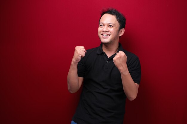 Happy excited and smiling young Asian man raising his arm up to celebrate success or achievement