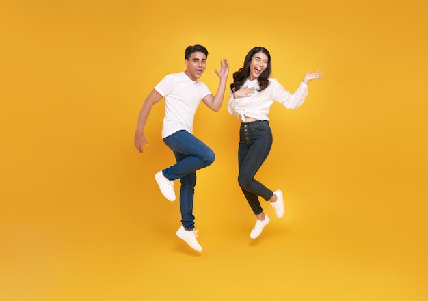 Happy excited young asian loving couple jumping isolated over yellow wall background