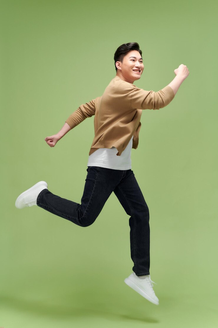 Photo 幸せな興奮した若いアジア人男性がグリーン スタジオの背景に分離されてジャンプ
