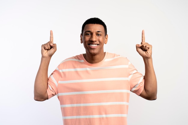 Happy excited young man looking at camera pointing up with fingers hand gesture at copy space