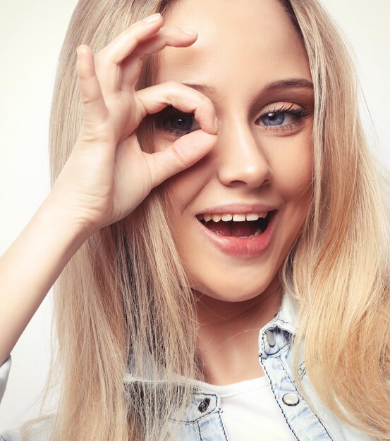 Happy excited young woman looking through hole made of her fingers over white background