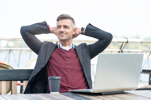 Uomo esecutivo felice che riposa dal lavoro durante la pausa caffè con il computer portatile nella caffetteria all'aperto