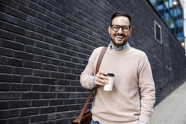 A happy executive in smart casual is holding coffee to go and smiling at the camera